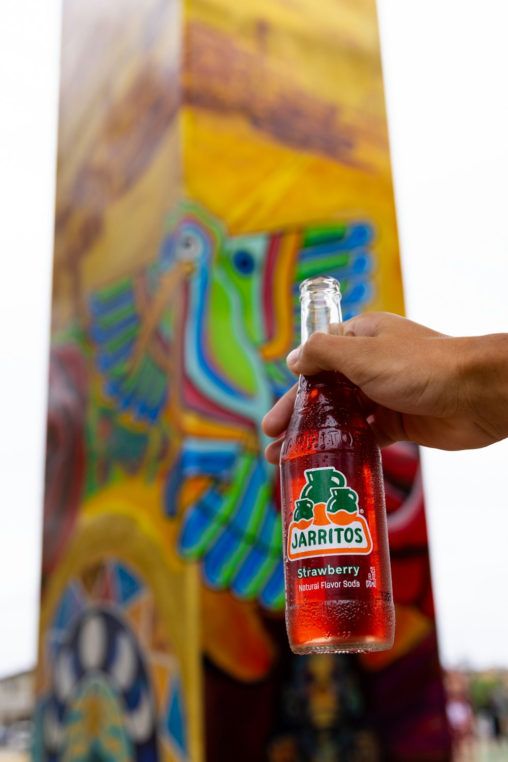 a person holding a bottle of beer in front of a colorful sculpture