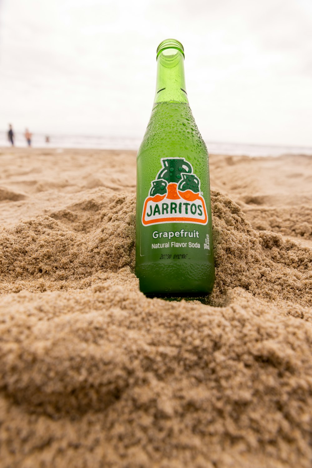 a bottle of beer sitting on top of a sandy beach