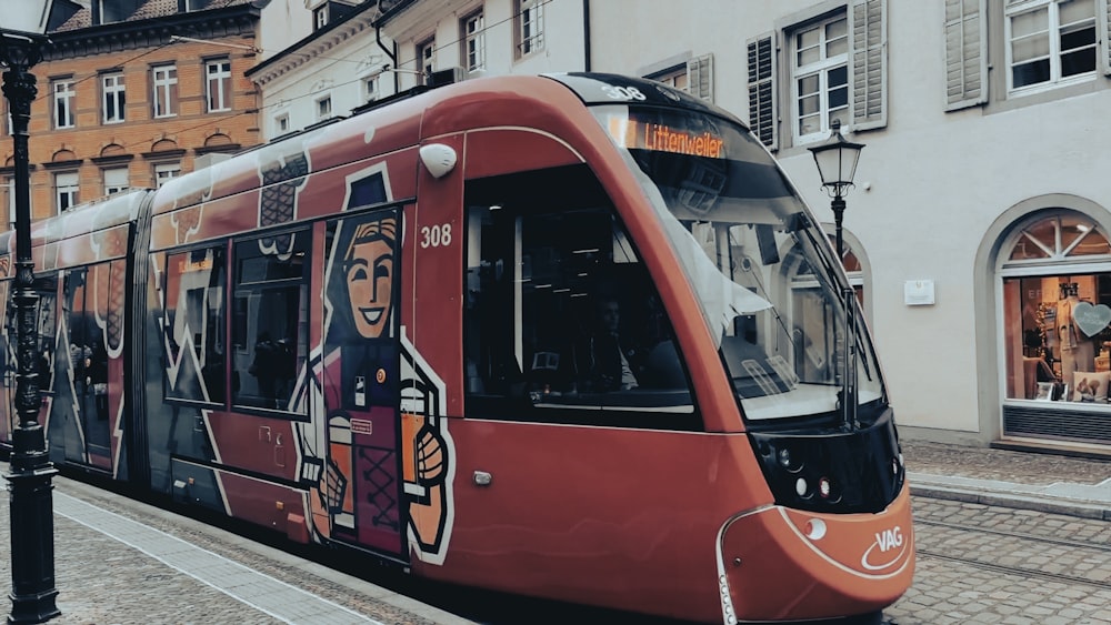 a red train traveling down a street next to tall buildings