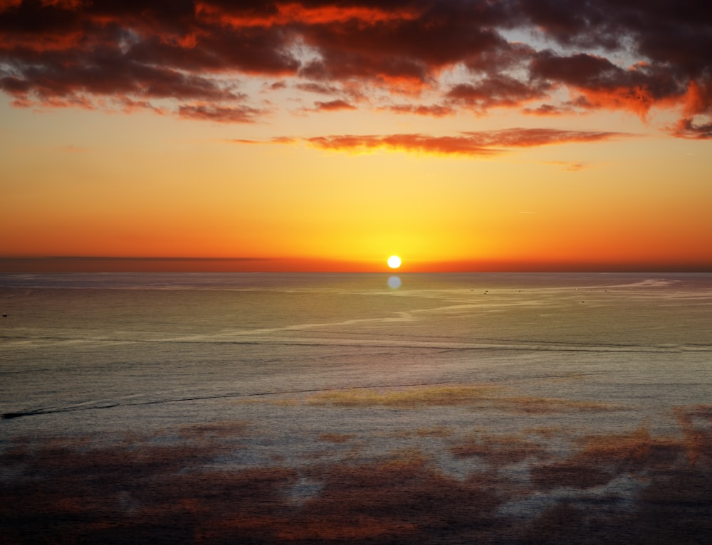 the sun is setting over the ocean on a cloudy day