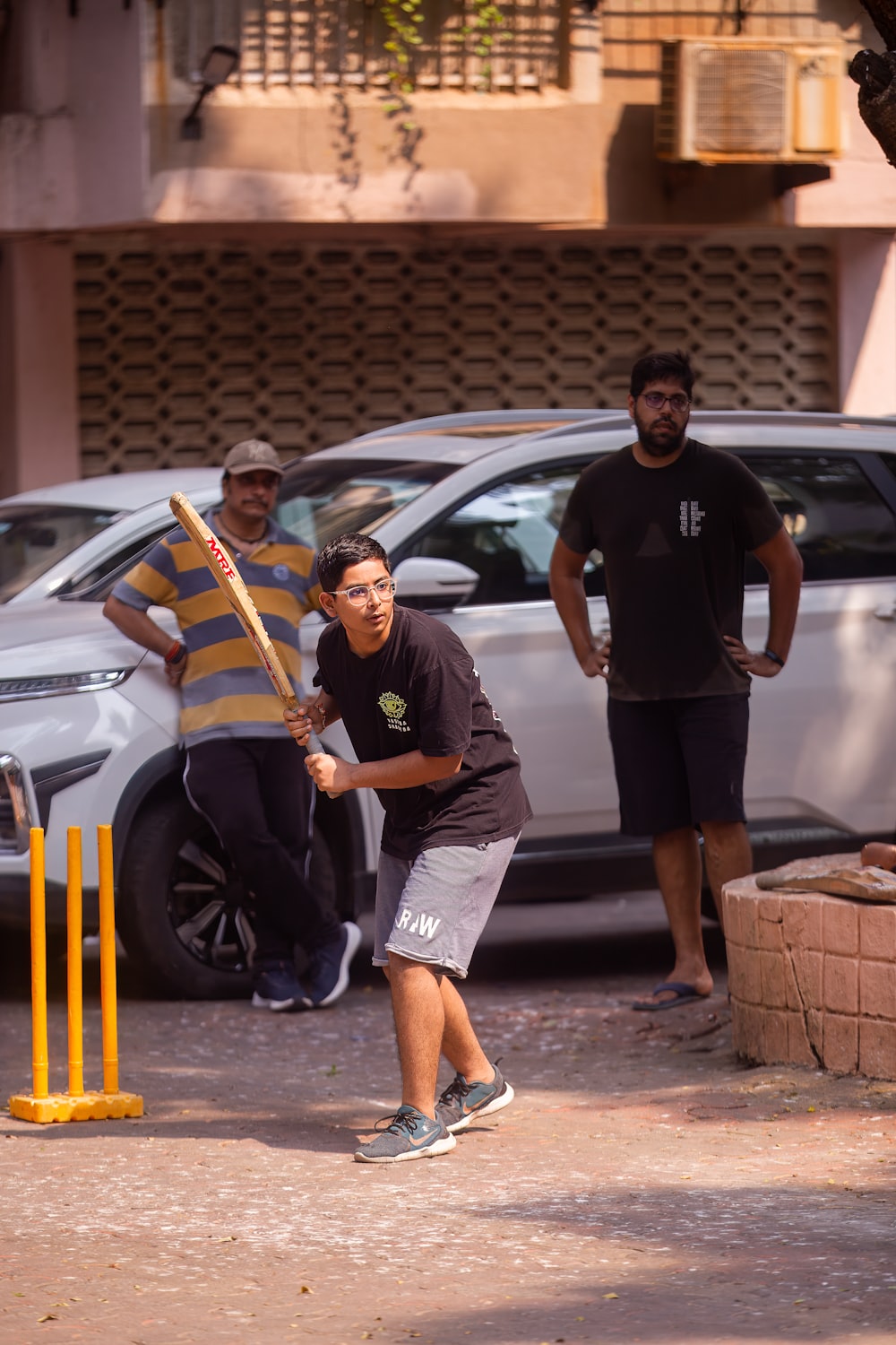 a young man holding a baseball bat next to a white car