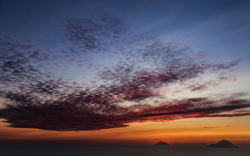 a sunset with clouds and mountains in the background