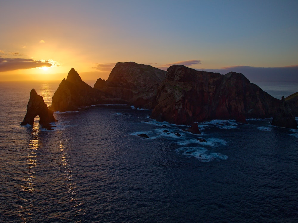 the sun is setting over the ocean with rocks in the foreground