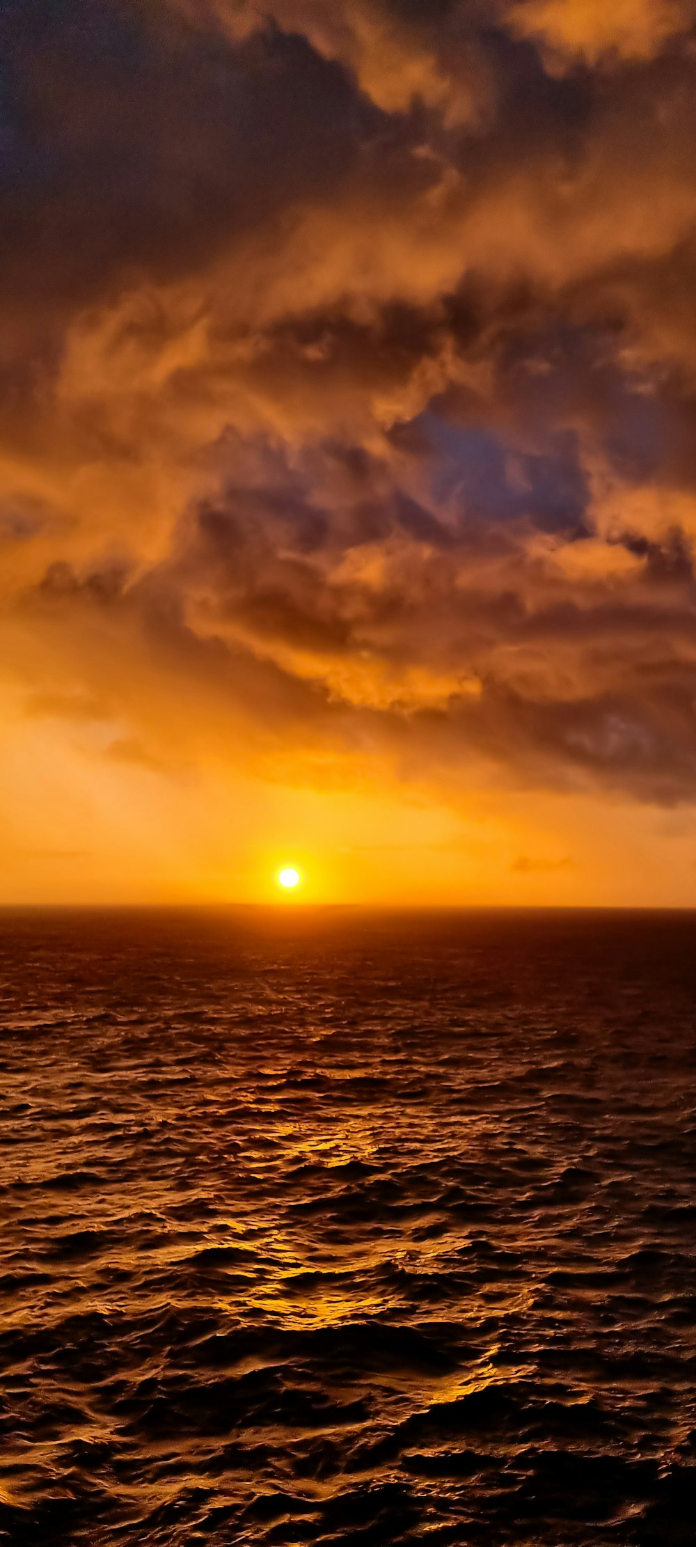 the sun is setting over the ocean on a cloudy day