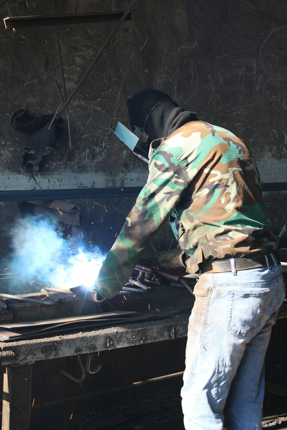 a man in camouflage jacket welding a piece of metal