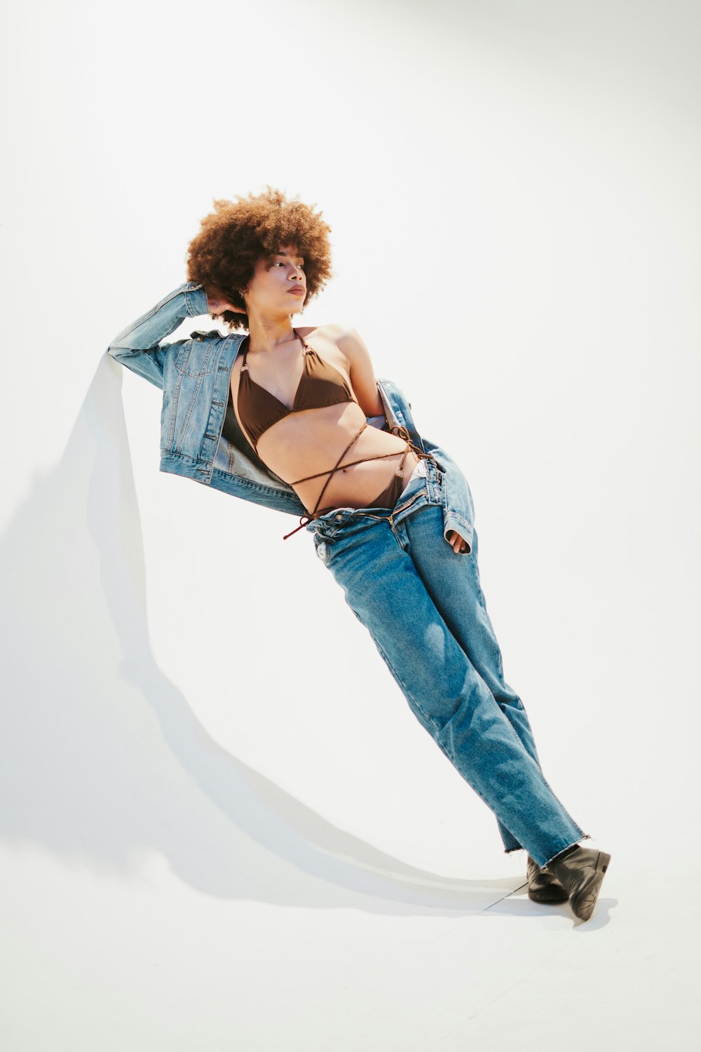 a woman in a bikini and jean jacket leaning against a wall