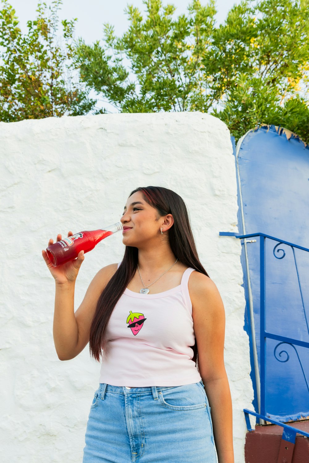 a woman standing in front of a white wall drinking from a red cup