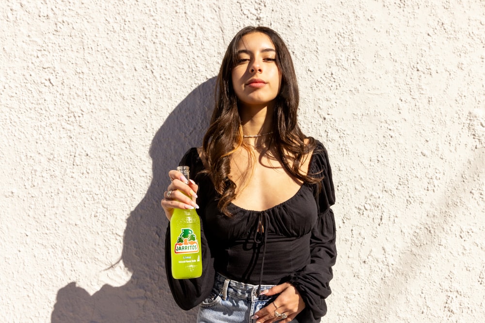 a woman standing next to a white wall holding a green bottle