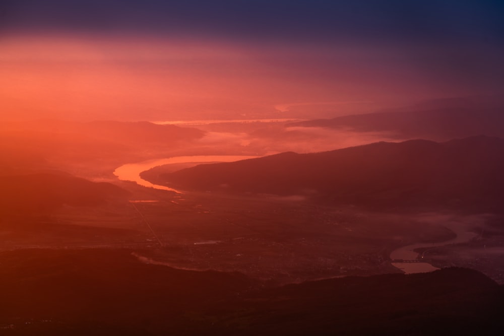 the sun is setting over a river and mountains