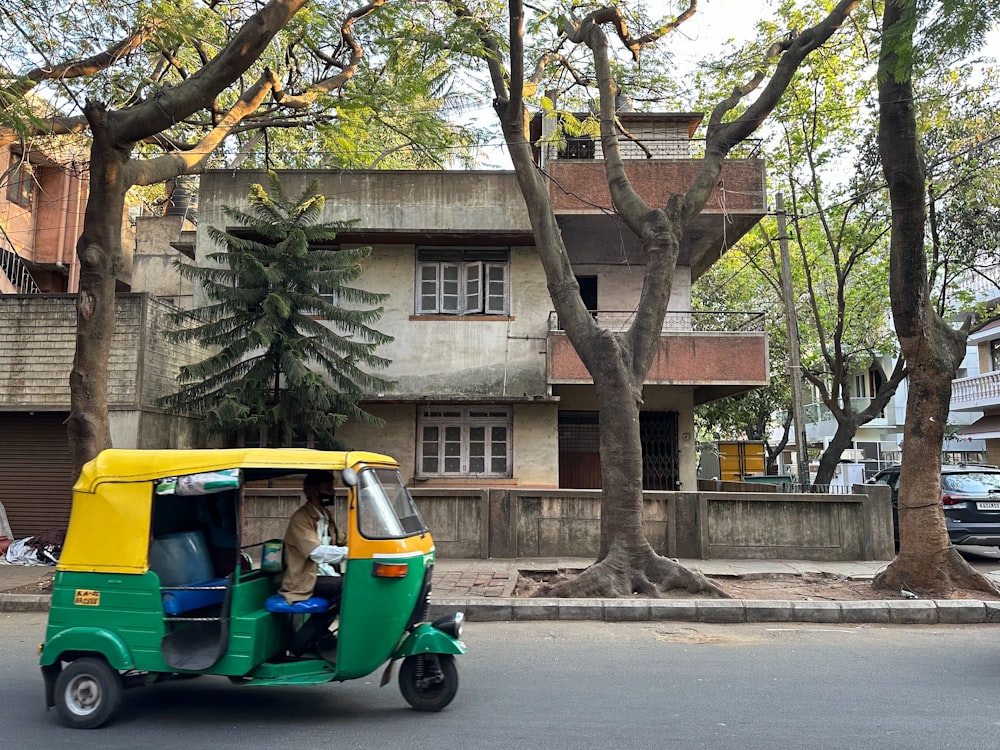 a man driving a green and yellow tuk tuk down a street