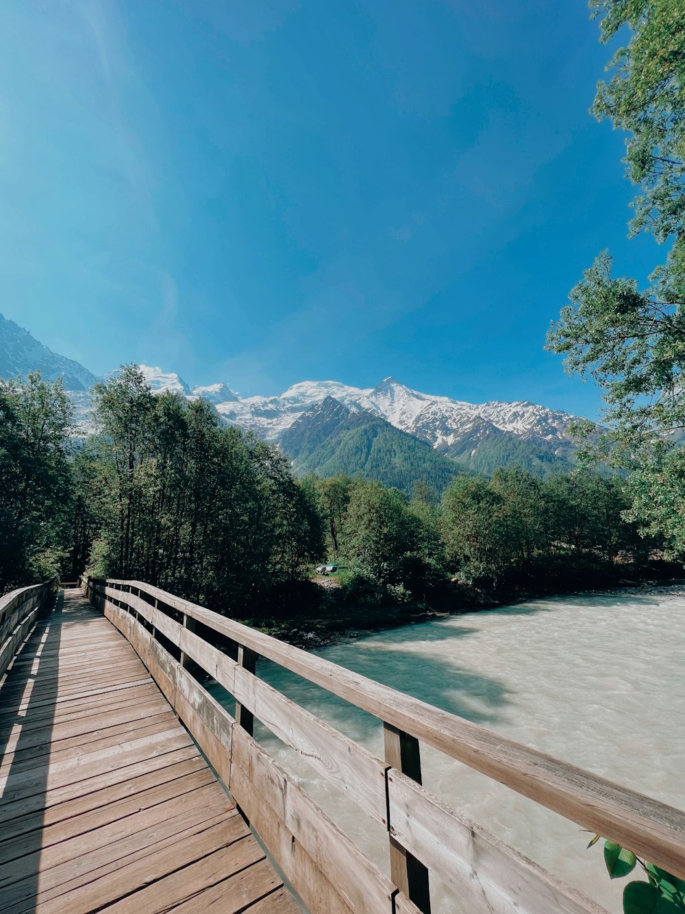 a wooden bridge over a river with mountains in the background