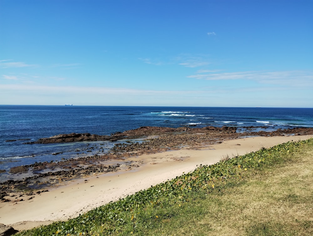 a sandy beach next to the ocean under a blue sky