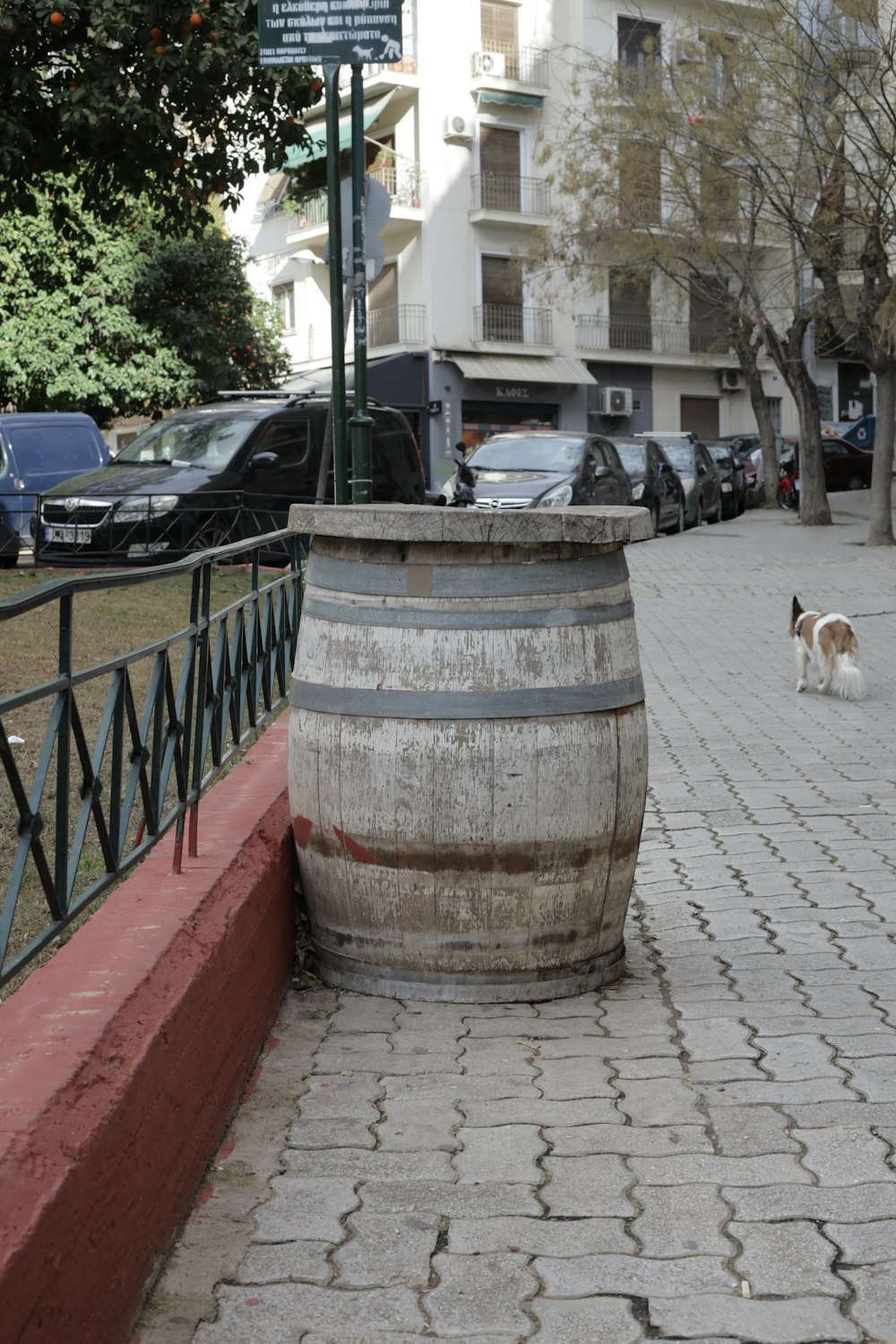 a dog walking on a sidewalk next to a barrel