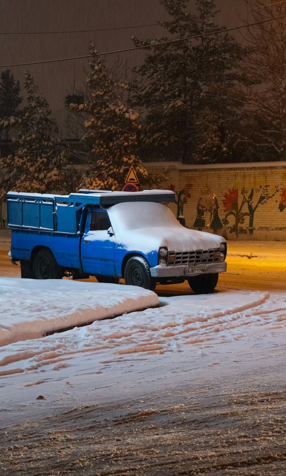 a blue truck parked on the side of a road covered in snow