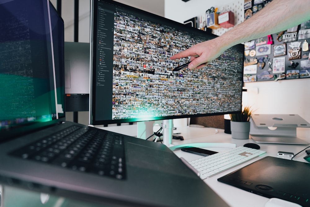 a person pointing at a computer screen on a desk