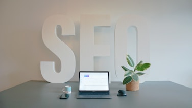 a laptop computer sitting on top of a desk with SEO sign on wall implying that Boomlytics offers SEO