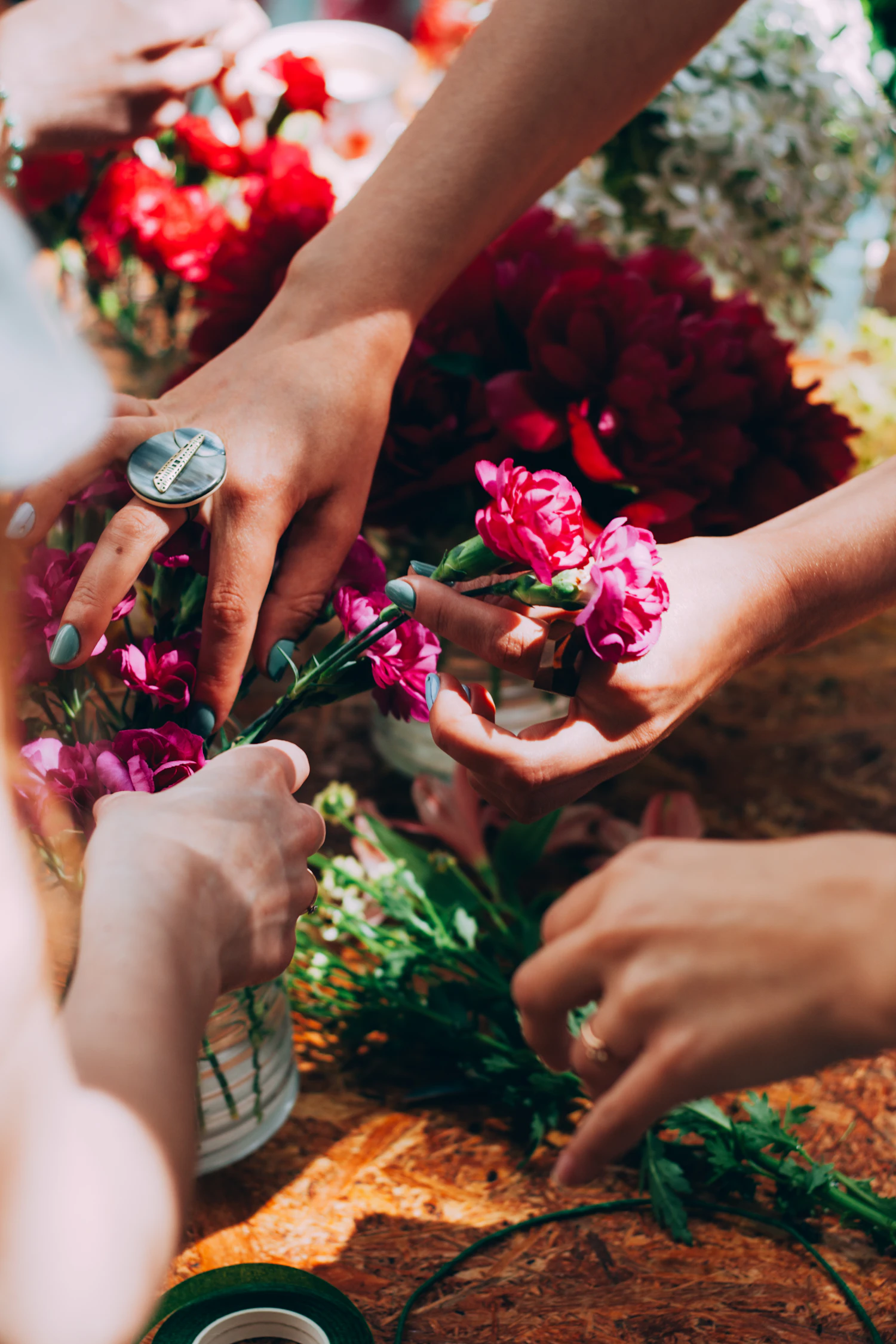 Several pairs of hands reaching across a bench covered in cut stems and offcuts