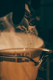 a person sprinkling sugar on top of a saucepan