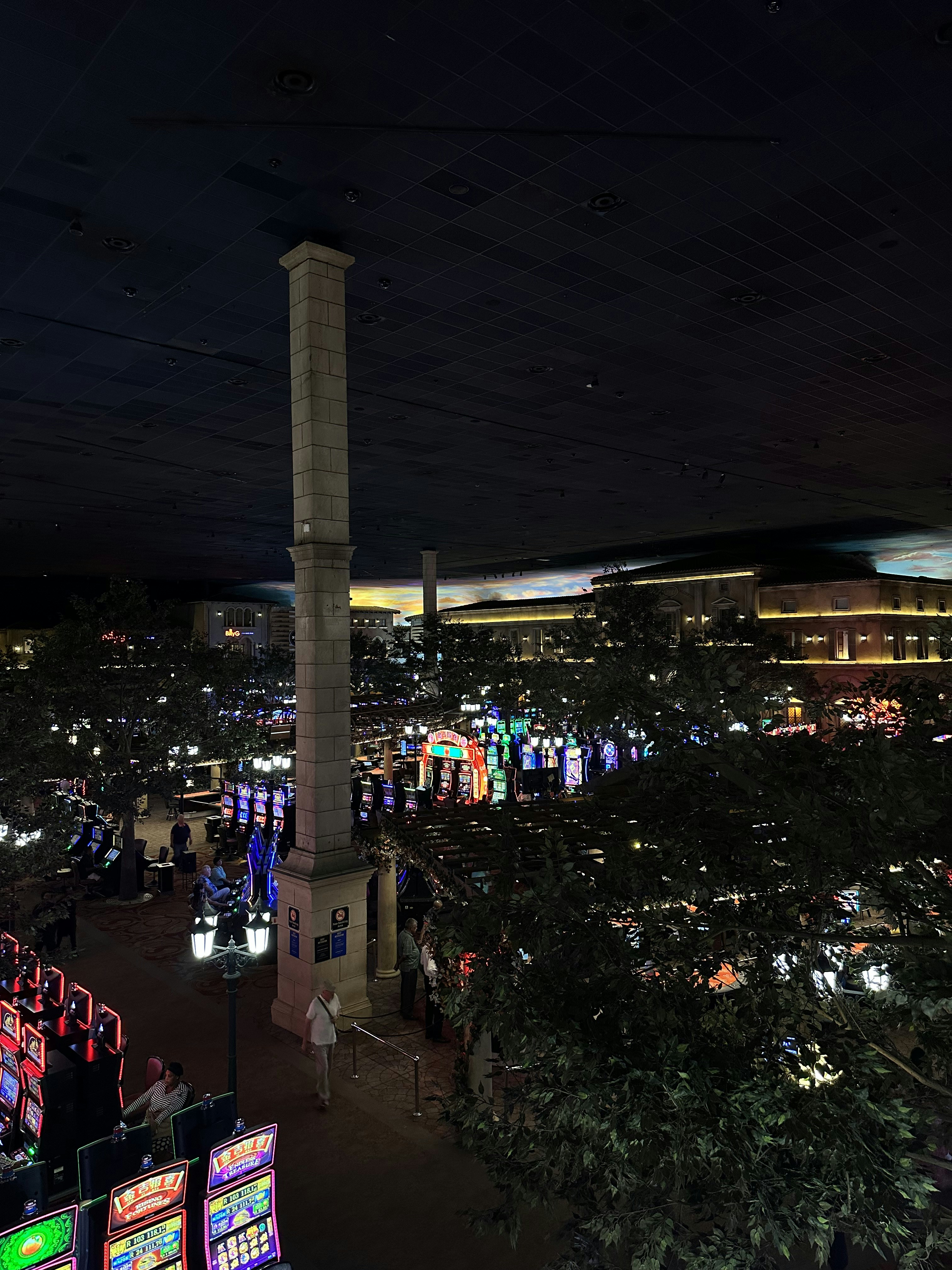 Bright modern casino gaming floor with rows of slot machines illuminated by colorful neon lights against a dark ceiling, empty aisles creating a sense of scale