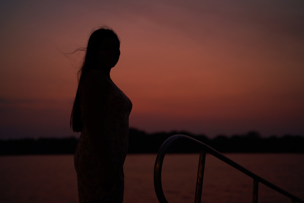 uma mulher em pé em um barco ao pôr do sol