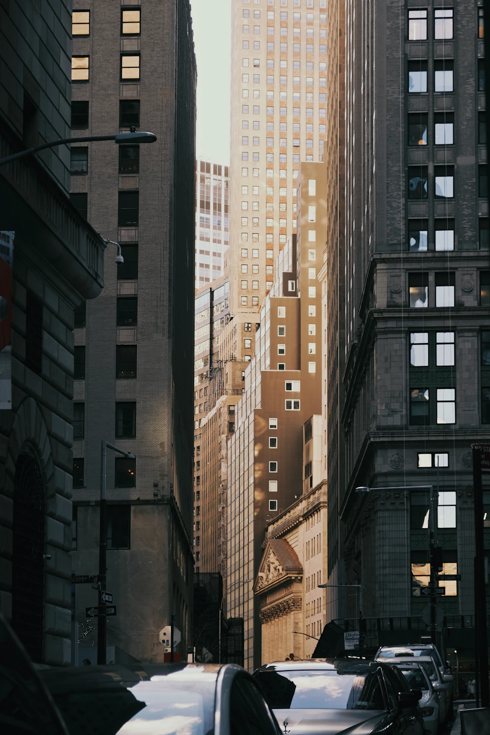 Bustling city street scene with tall buildings and reflected sunset glow from ground level