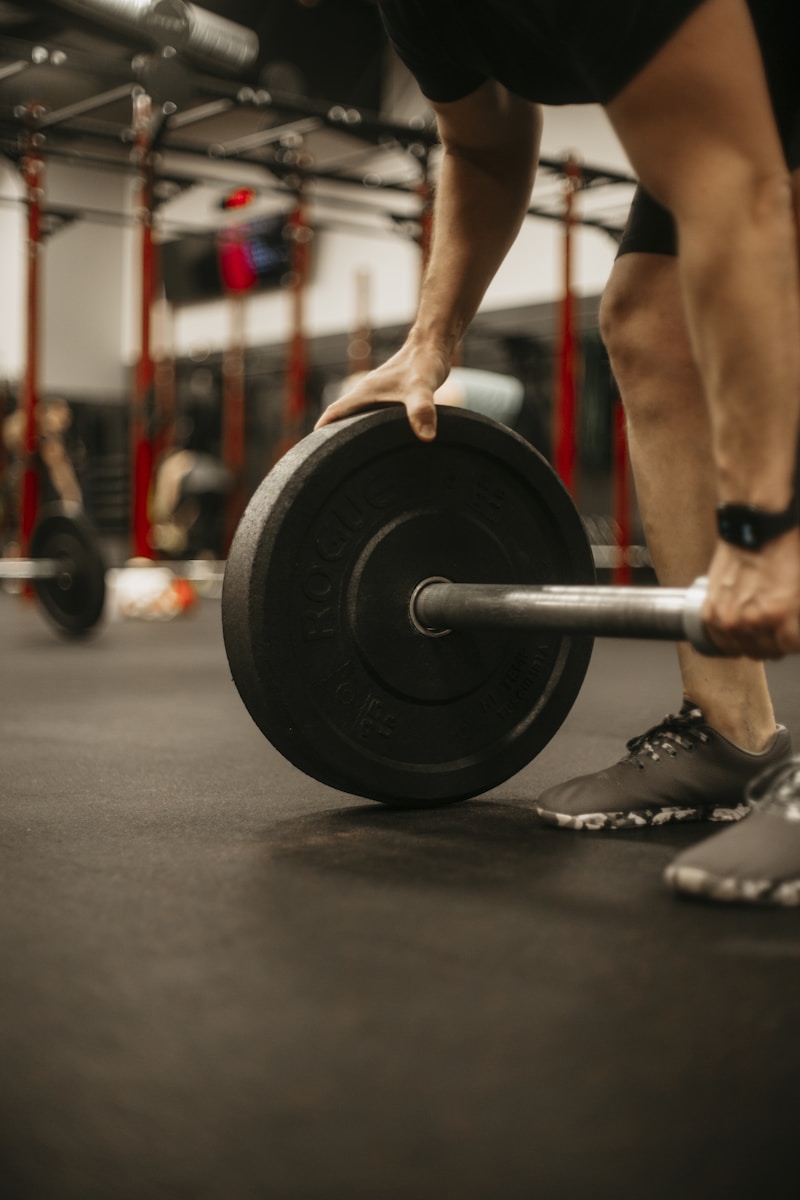 Lifter steadying a bumper plate on a barbell in a rig-lined gym