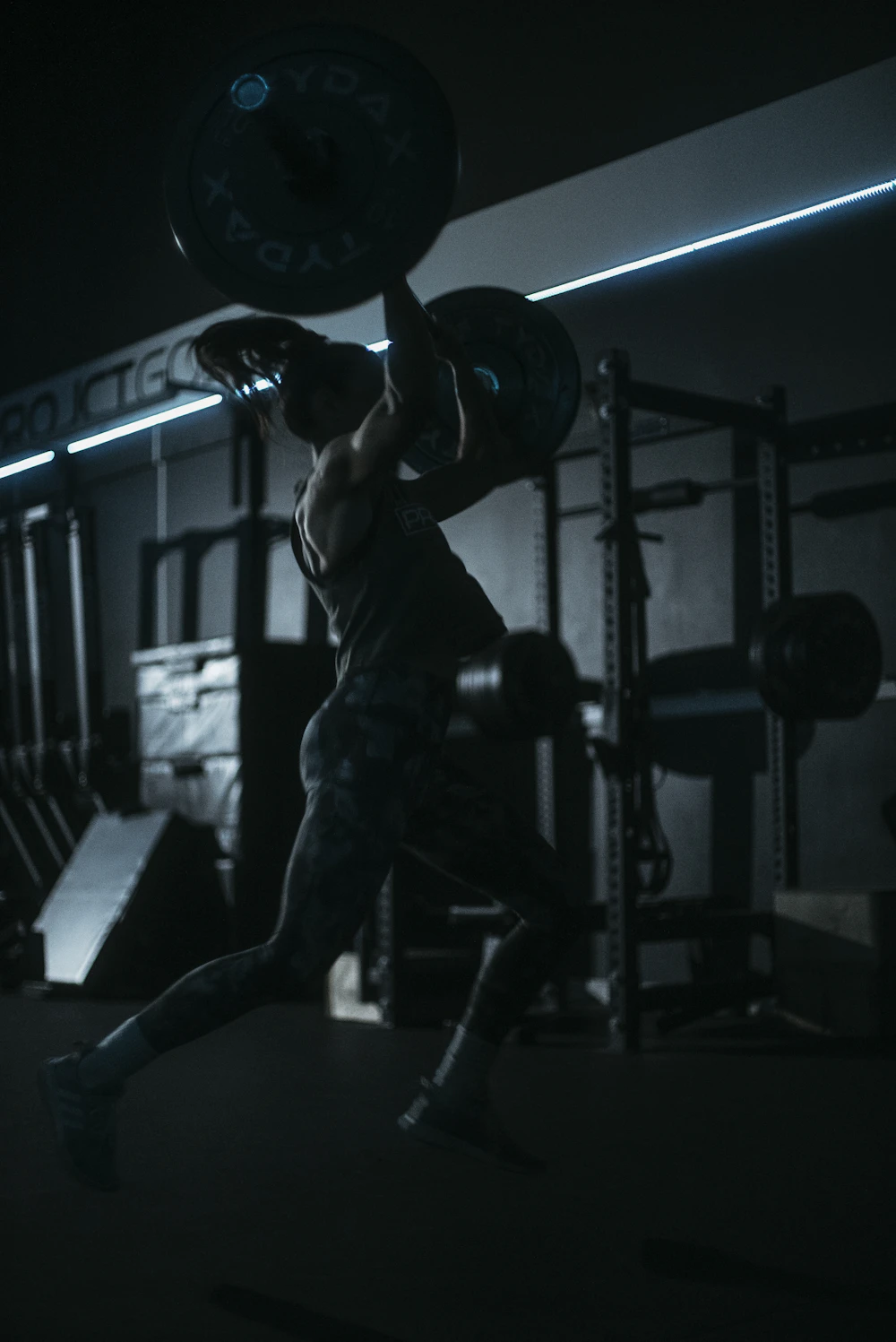 A lone lifter mid-set, silhouetted in a dark, dramatically lit gym