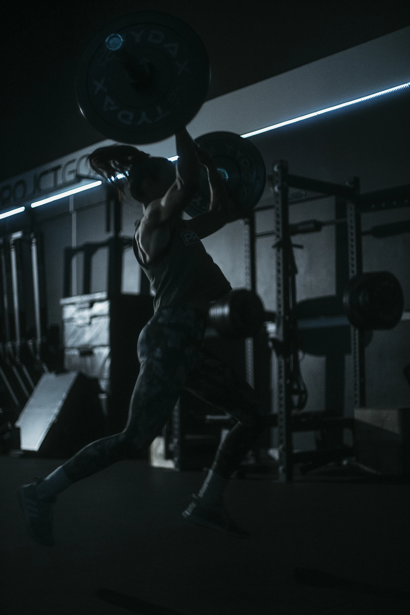 An athlete braced under a loaded barbell in a dark gym, mid-lift