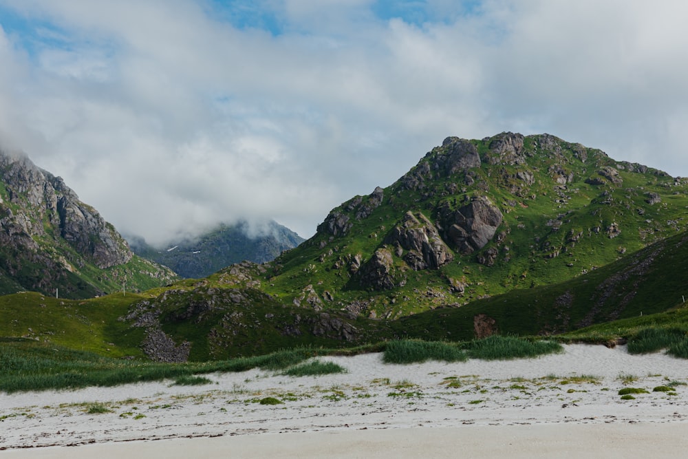 a mountain range covered in green grass and clouds