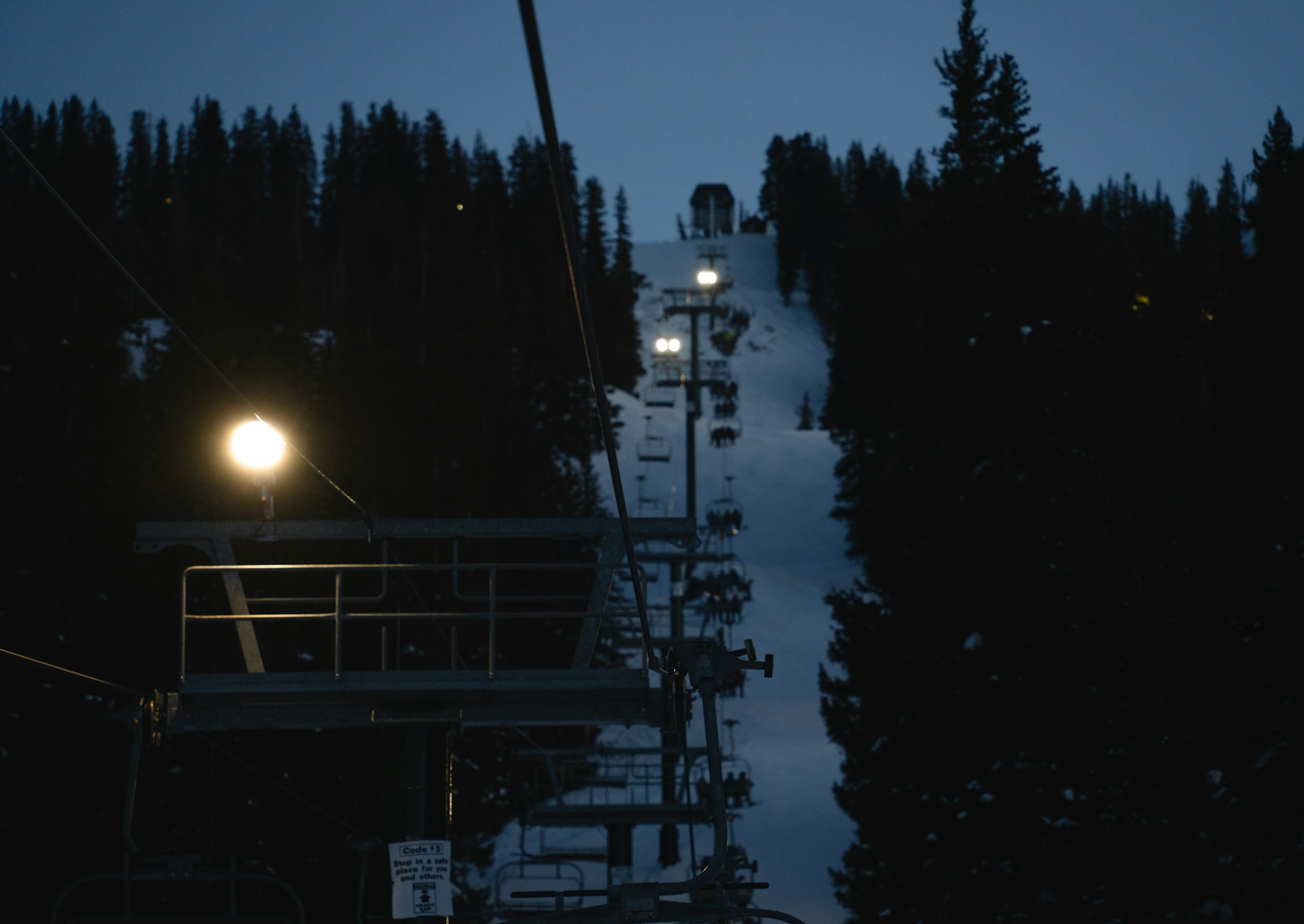 A ski lift going up a snowy hill at night