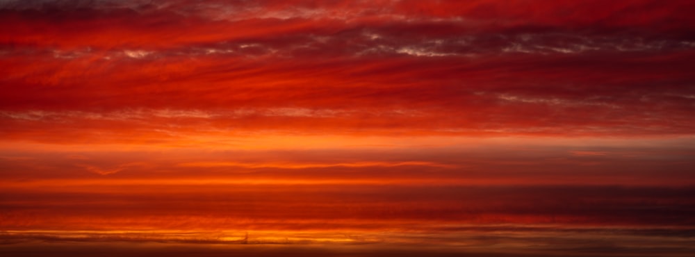 a red sky with clouds and a plane in the distance