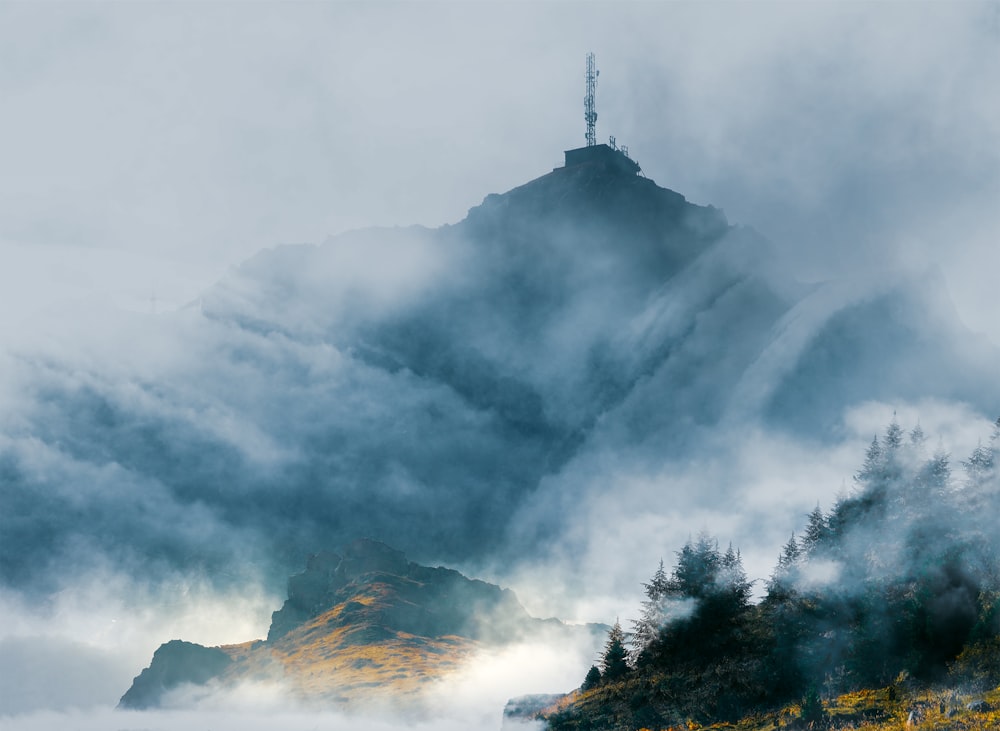 une montagne couverte de brouillard surmontée d’une croix
