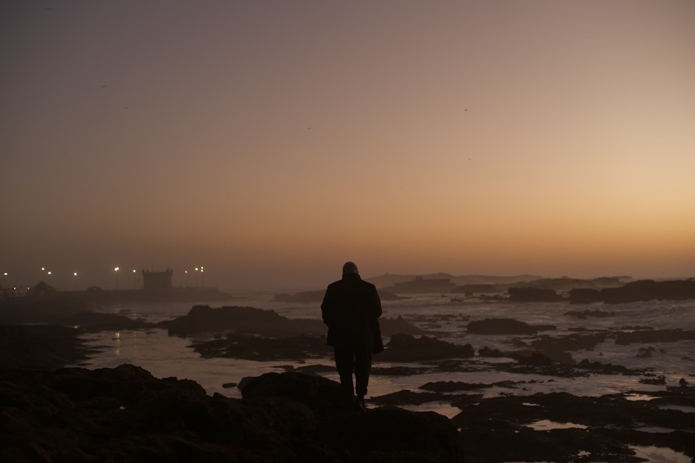 a person standing on a rocky beach at sunset