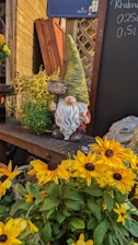 a garden gnome sitting on a bench surrounded by sunflowers
