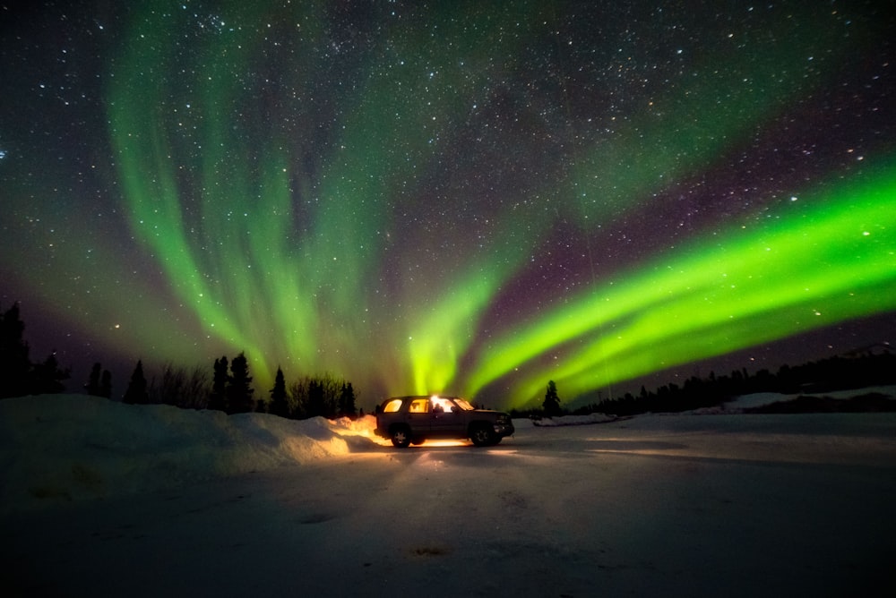 a truck driving down a snow covered road under a green and purple sky