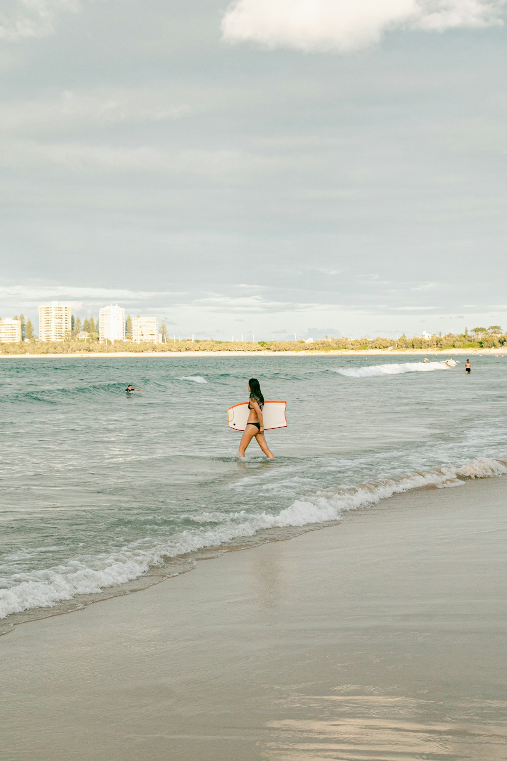 a woman walking into the ocean with a surfboard