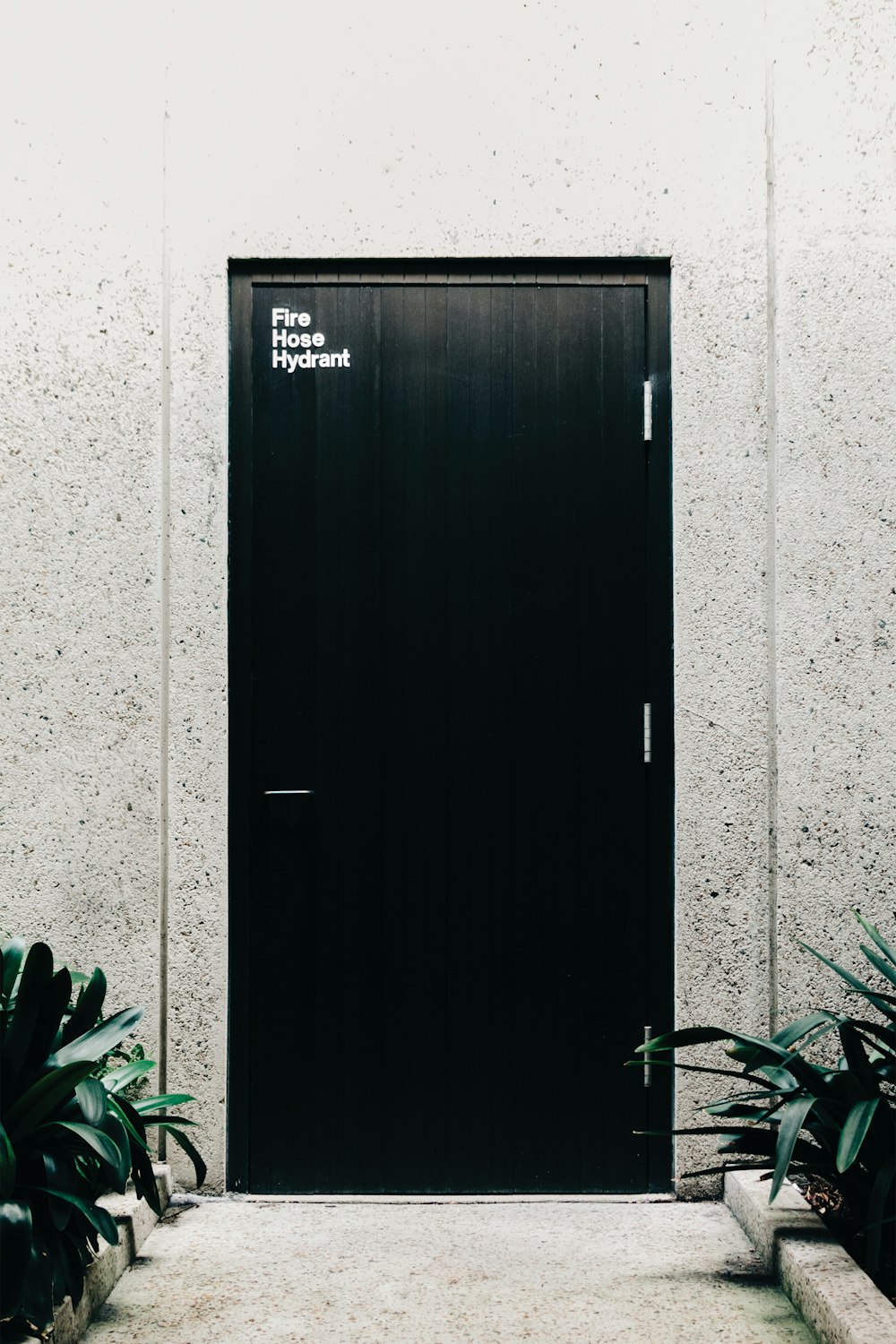 a black door with a sign on it next to some plants