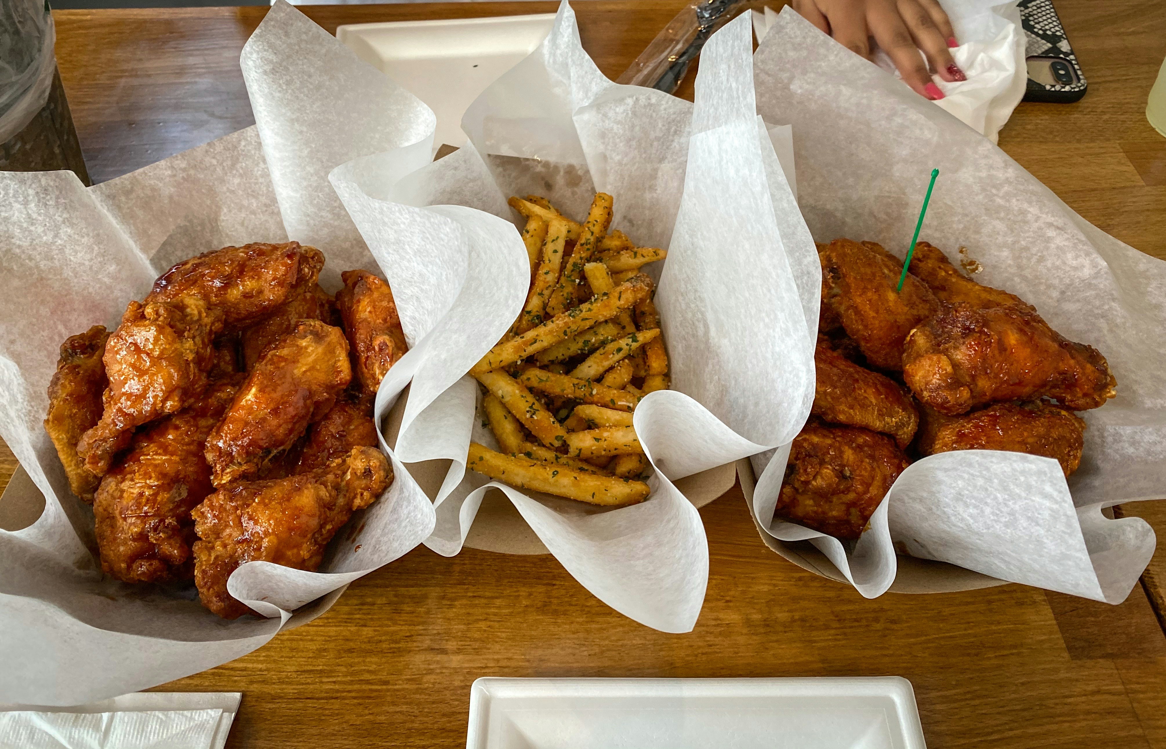 a wooden table topped with baskets filled with chicken wings and french fries
