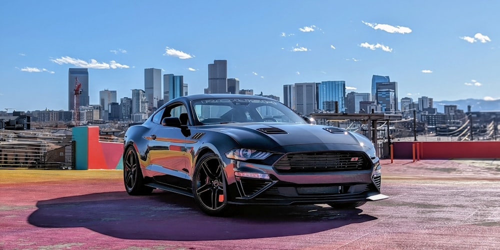 a black mustang parked in front of a city skyline