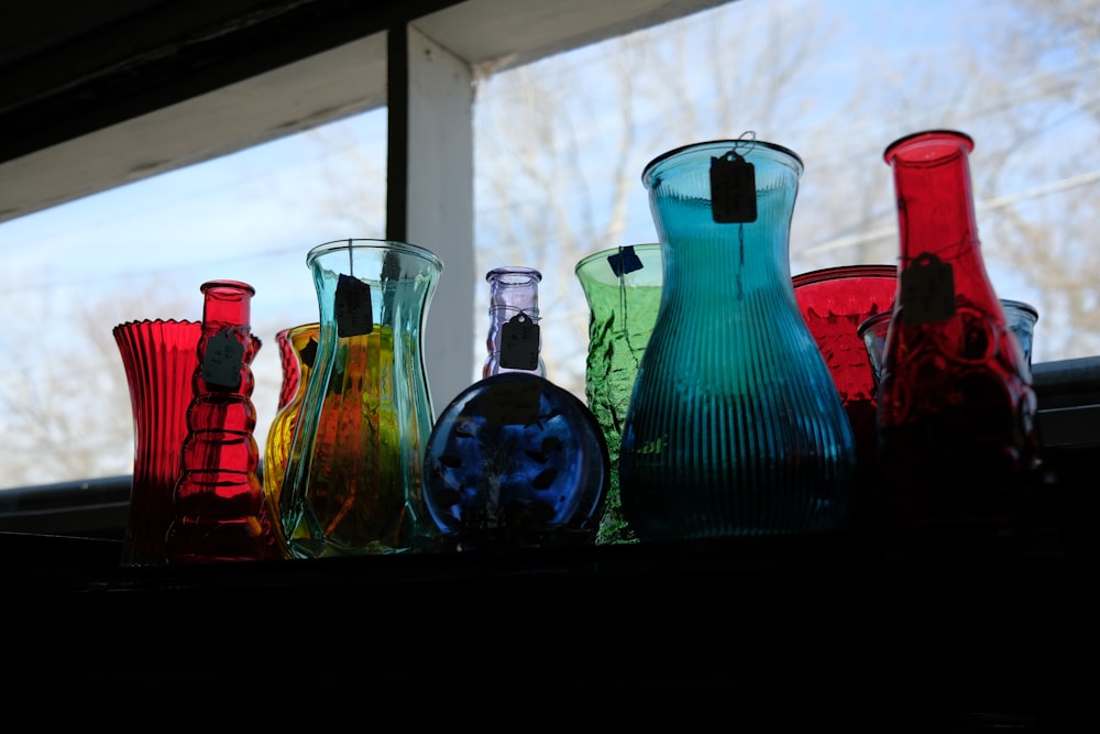 a group of different colored vases sitting on a window sill