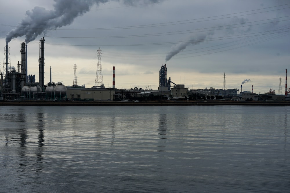 smoke billows from a factory near a body of water