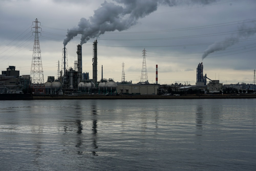 smoke billows from a factory near a body of water