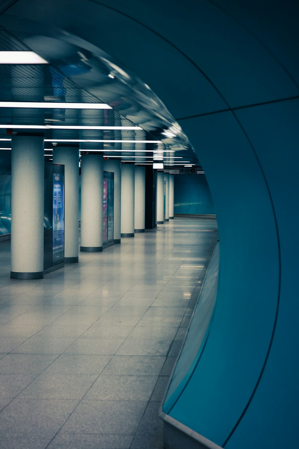 uma estação de metrô vazia com paredes azuis e colunas brancas