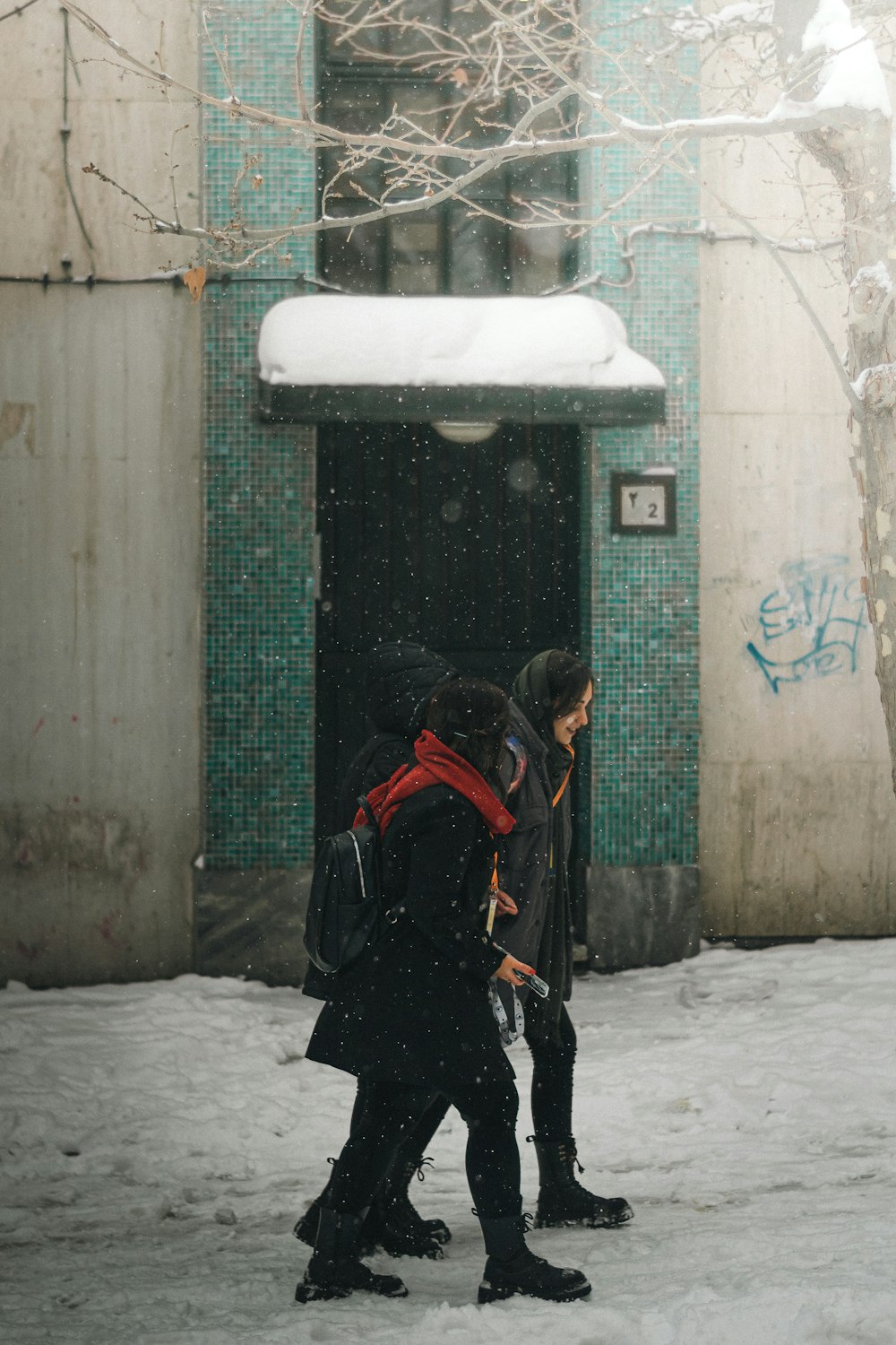 two people walking in the snow in front of a building