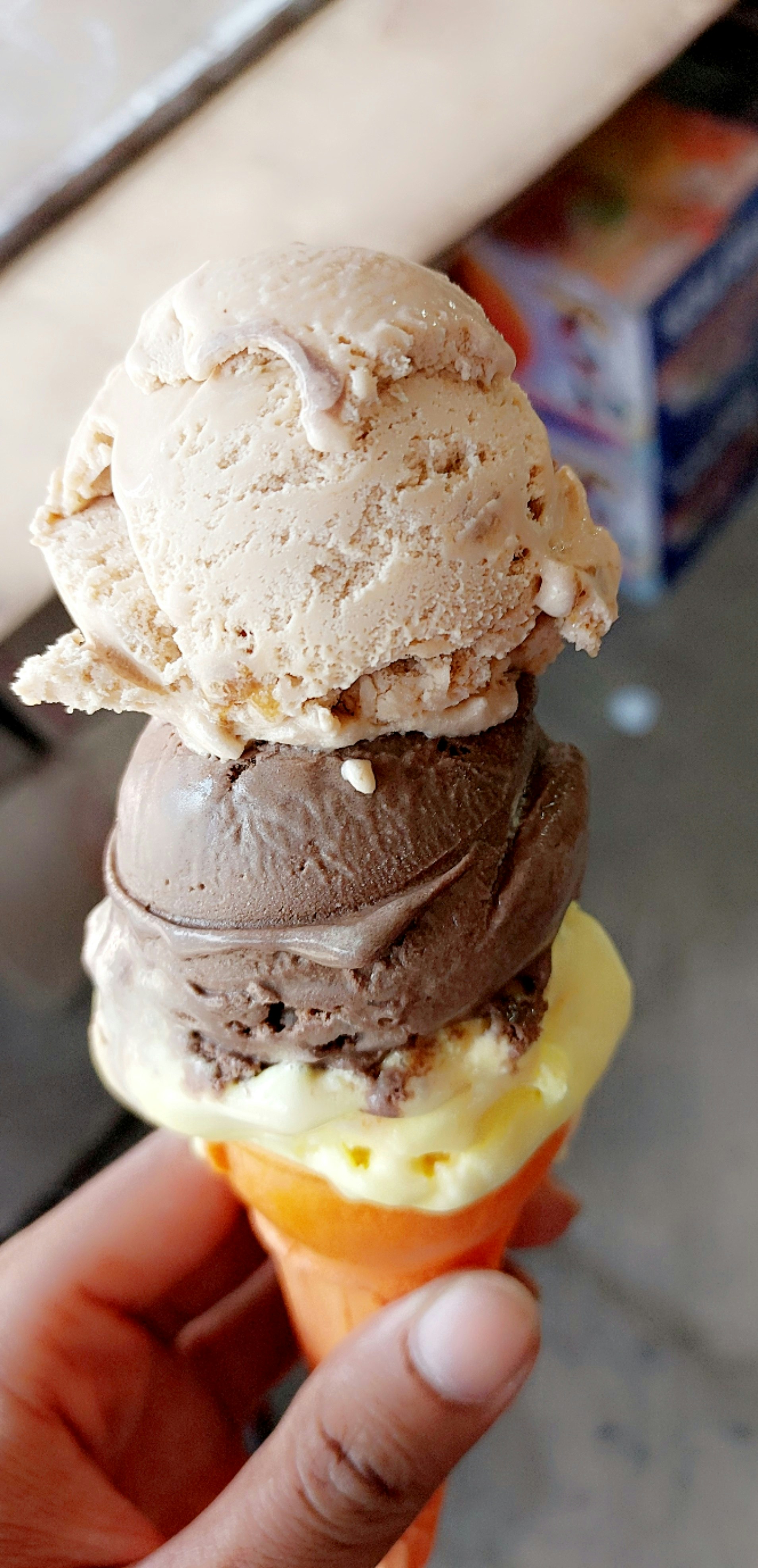 uma mão segurando uma casquinha de sorvete recheada com chocolate e baunilha