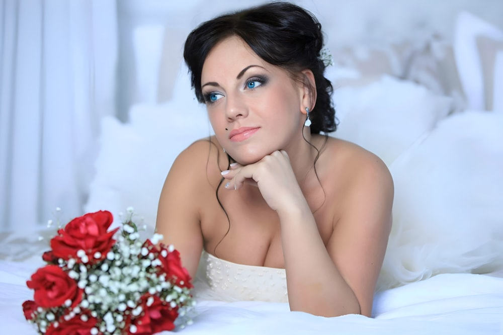 a woman laying on top of a bed next to a bouquet of flowers