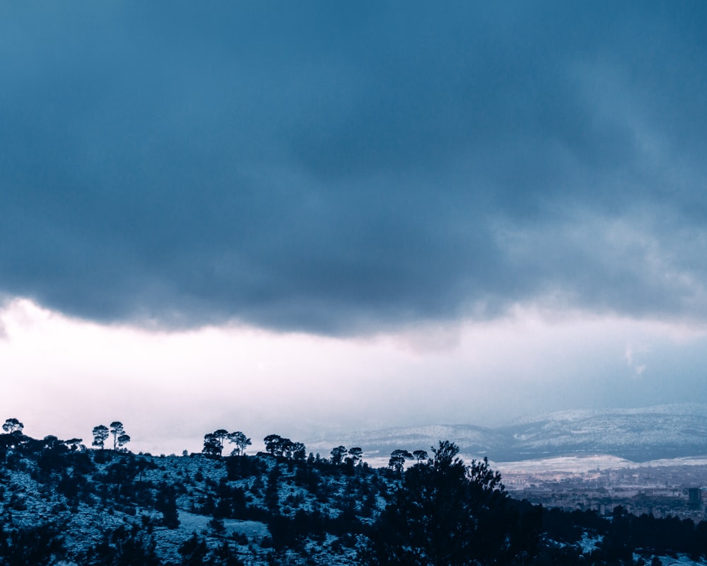 a cloudy sky over a mountain with trees