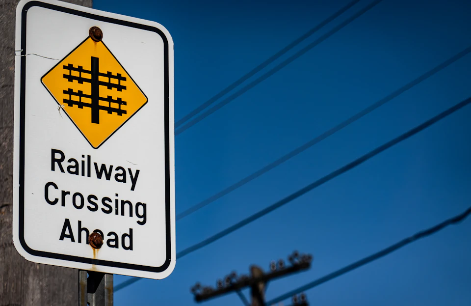 White rectangular traffic sign with "Railway Crossing Ahead" and yellow diamond symbol attached to pole