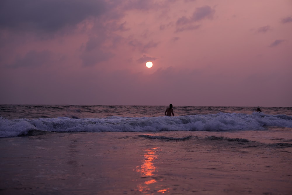 a person standing on a surfboard in the ocean at sunset