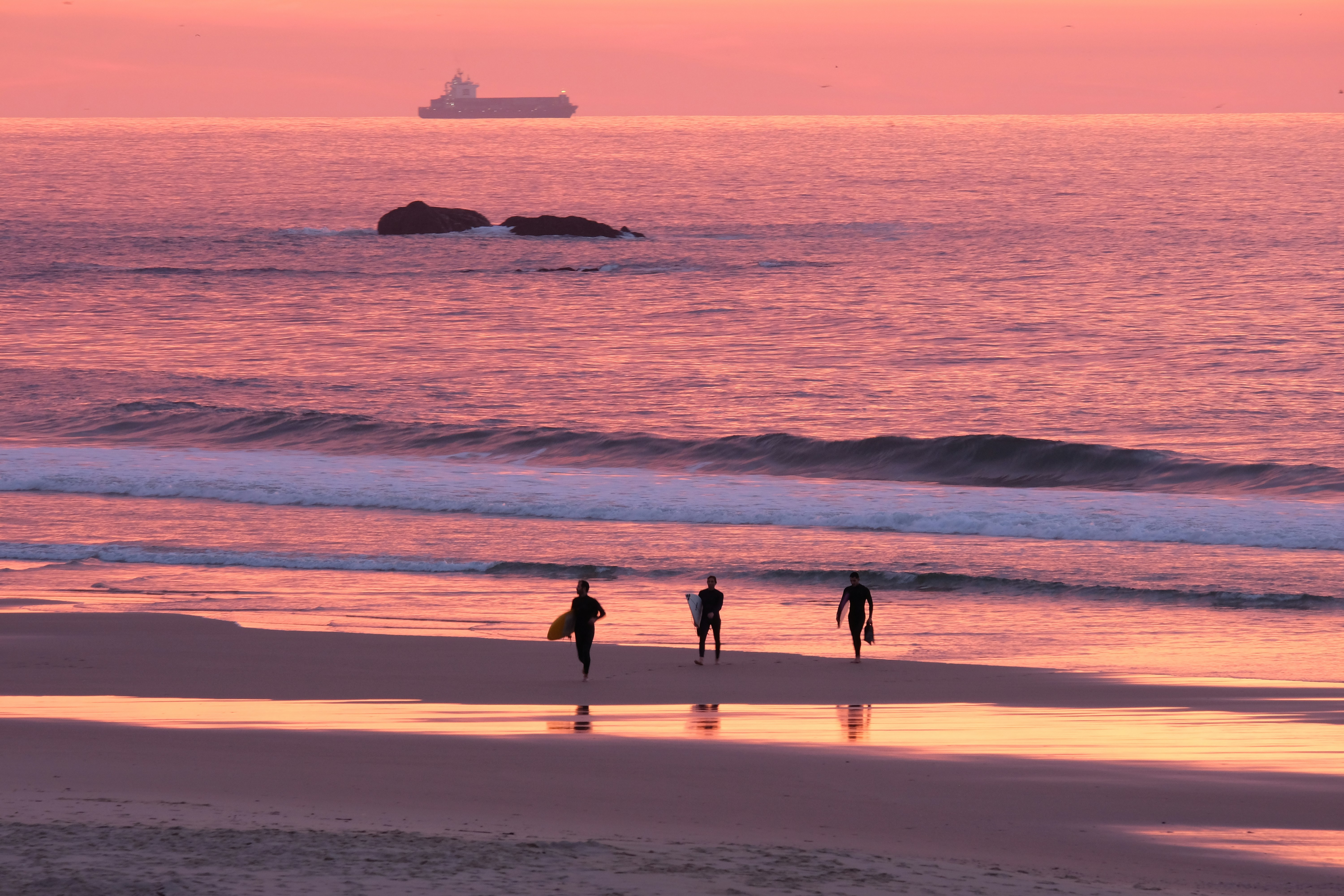Três pessoas estão caminhando na praia ao pôr do sol